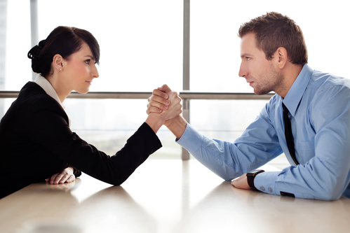 Businessman and businesswoman arm wrestling on desk in office
